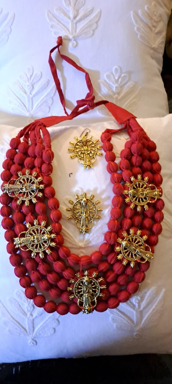 Red beaded necklace with gold pendants on a white textured surface